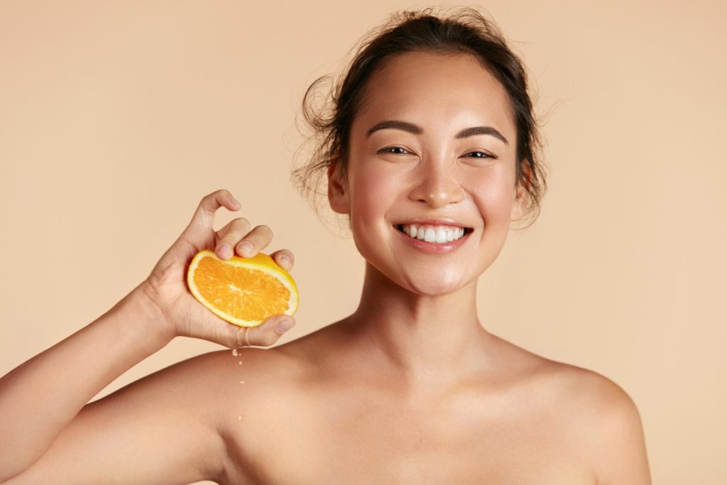 beauty. woman with radiant face skin squeezing orange portrait